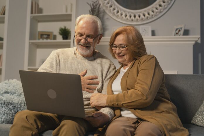 elderly couple sitting on a couch while in a video call using a laptop